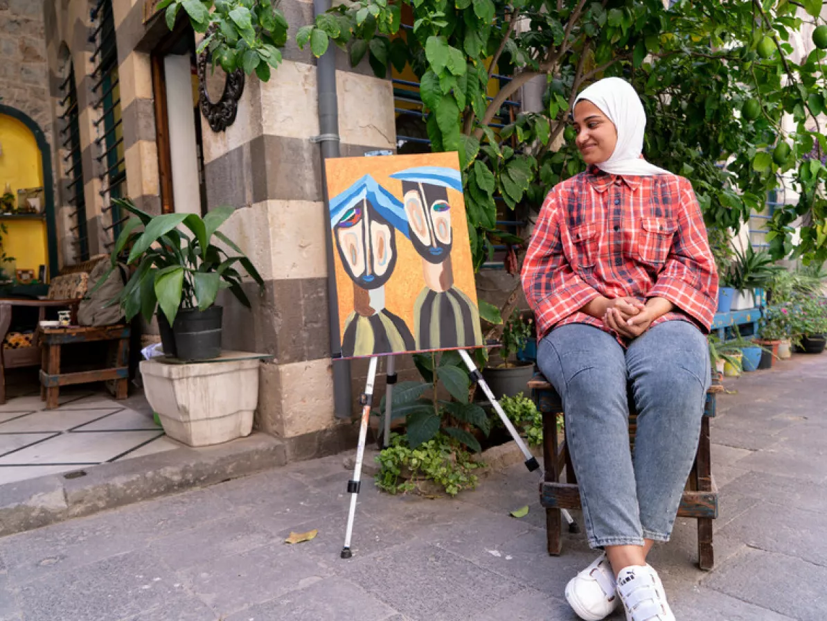 Aya Abdullah Fadi, 21, with her painting, ”Two Prisoners” that appeared in the Beyond Colors art exhibition in Homs, Syria.